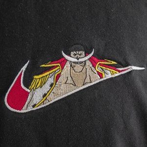 Peut inclure: T-shirt noir avec un logo Nike swoosh rouge et blanc représentant un personnage de dessin animé avec une moustache et une cape rouge.