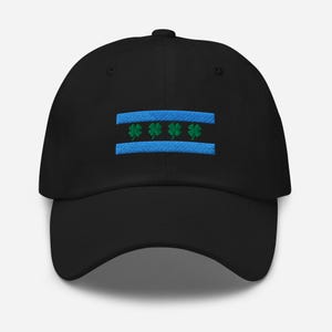 May include: Black baseball cap with a blue and green embroidered design. The design features two horizontal blue stripes with four green shamrocks in the center. The cap has a curved brim and a button on top.