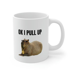 May include: White ceramic mug with a black and white image of a capybara wearing sunglasses and a gold chain with a dollar sign charm. The text "OK I PULL UP" is printed in black above the image.