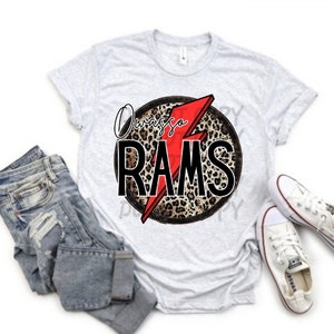 May include: A white t-shirt with a black and brown leopard print circle with a red lightning bolt and the text "Always a RAMS" in black.