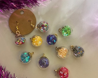 May include: Assortment of 10 small glass ornaments with gold tops and filled with colorful glitter. The ornaments are arranged on a white surface.