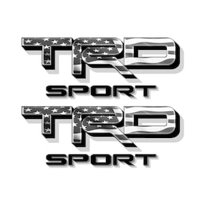 Puede incluir: Dos calcomanías TRD Sport. Las letras TRD están rellenas con un patrón de estrellas blancas sobre un fondo oscuro. La letra D tiene un patrón de rayas. La palabra SPORT está debajo de las letras TRD.