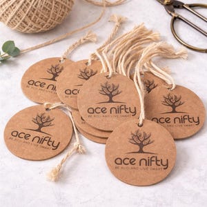 May include: A collection of round, brown paper tags with the text "ace nifty" and a tree logo, strung with natural twine. A ball of twine and scissors are also visible, suggesting a craft or eco-friendly product theme.