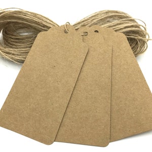 May include: Three brown kraft paper gift tags with a hole punched in the top. The tags are stacked on top of each other and are surrounded by a ball of twine.