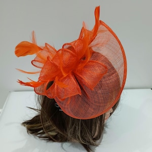 May include: Orange mesh fascinator with a large bow and feathers.