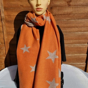May include: A soft orange scarf with a fringe border and a pattern of large grey stars.
