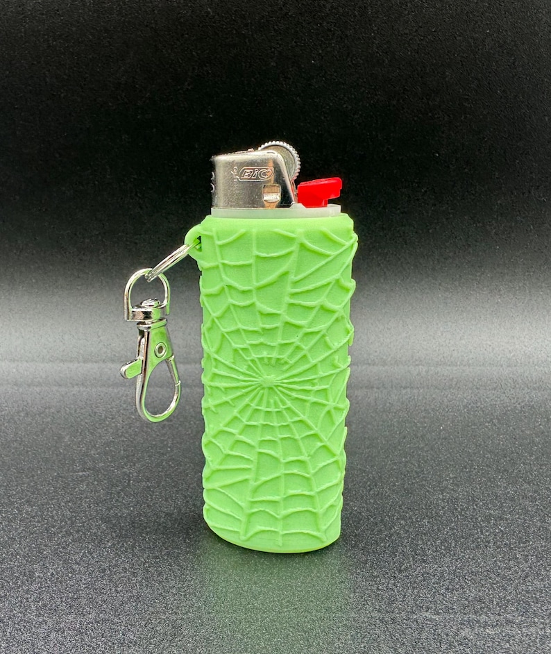 May include: A green lighter with a spiderweb design and a silver keychain attached. The lighter has a red button and the text "BIC" is visible on the side.