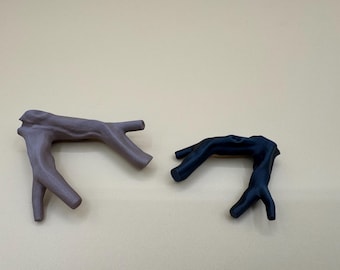May include: Two decorative branch-shaped objects. One is a muted purple color, and the other is a deep navy blue. The objects have a naturalistic, organic form, with multiple protruding branch-like elements. They are placed against a neutral background.