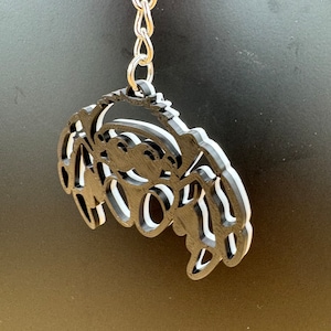 Könnte beinhalten: Ein mehrschichtiger Schlüsselanhänger in Form einer Krabbe in Schwarz und Weiß. Der Schlüsselanhänger ist an einer silbernen Kette befestigt.