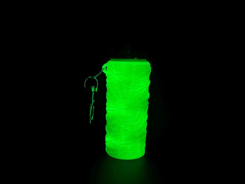 May include: A green glow-in-the-dark bottle with a key chain attached. The bottle is made of a textured material and has a round shape.