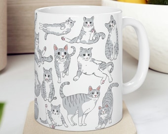May include: White ceramic mug with a pattern of gray and white cats in various poses. The mug has a handle on the right side.
