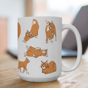 May include: White ceramic mug featuring a design of orange tabby cats in different poses. The cats are outlined in black and have white markings.