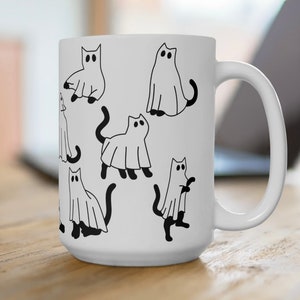 May include: White ceramic coffee mug with a black and white illustration of cats dressed as ghosts. The mug has a large handle.
