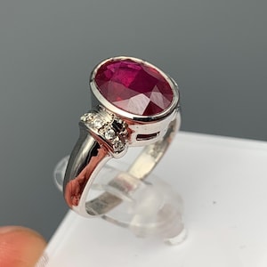 Könnte beinhalten: Ein silberner Ring mit einem großen ovalen Rubin-Edelstein und kleineren Diamant-Akzenten.