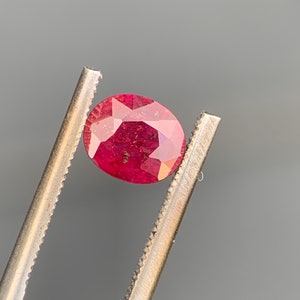 Op de afbeelding: Een dieprode ovale edelsteen vastgehouden door een pincet. De edelsteen is facetgeslepen en is een robijn.
