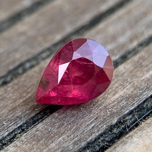 Peut inclure: Une pierre précieuse de rubis de forme poire avec une couleur rouge foncé. La pierre précieuse est facetée et a un haut poli.
