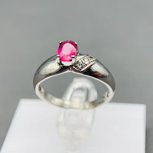 Könnte beinhalten: Ein silberner Ring mit einem rosafarbenen ovalen Edelstein und kleineren klaren Edelsteinen auf der Ringschiene.