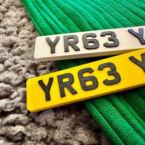 May include: Two number plates, one white and one yellow, with the letters "YR" and the numbers "63" and the letter "Z" printed in black.