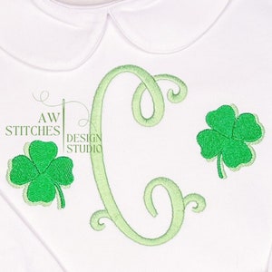 May include: Green embroidered shamrock design with a green cursive letter C. The design is on a white fabric background.