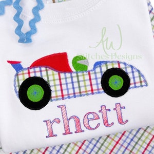 May include: A white t-shirt with a red, blue, and green plaid race car applique. The car has a green driver and the name "Rhett" is embroidered below the car in pink.