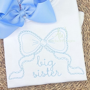 May include: White baby onesie with blue embroidered text that says "big sister" and a blue embroidered bow with a scalloped edge.