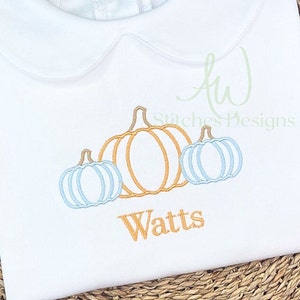 Puede incluir: Un pelele blanco con un diseño bordado de tres calabazas. Las calabazas son naranja, azul y azul claro. El nombre "Watts" está bordado debajo de las calabazas.