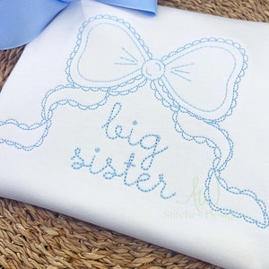 May include: White embroidered baby onesie with a blue bow and the text "big sister" in blue thread.