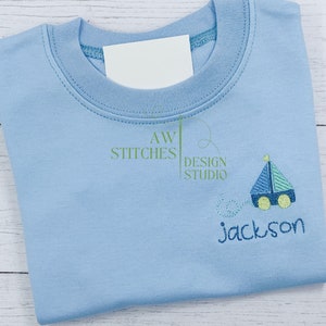 Pu&ograve; includere: Maglietta blu chiaro con un design di barca a vela blu e verde e il nome "Jackson" ricamato sul davanti.