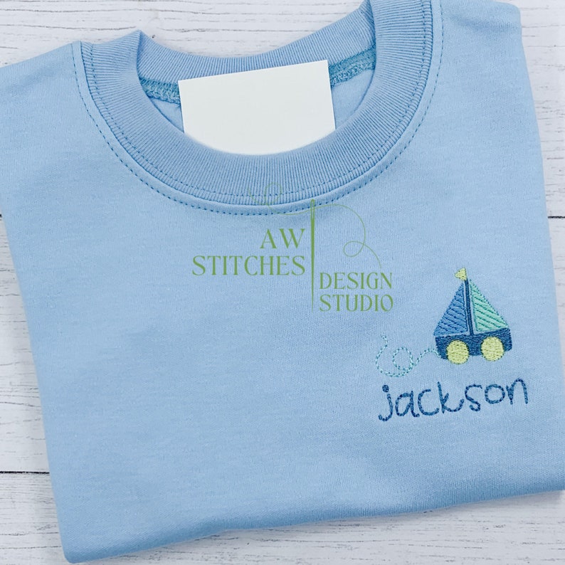 Pu&ograve; includere: Maglietta blu chiaro con un design di barca a vela blu e verde e il nome "Jackson" ricamato sul davanti.