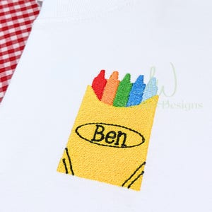 May include: White t-shirt with an embroidered design of a yellow crayon box. The crayon box contains red, orange, green, blue, and light blue crayons. The name "Ben" is embroidered on the crayon box in black.