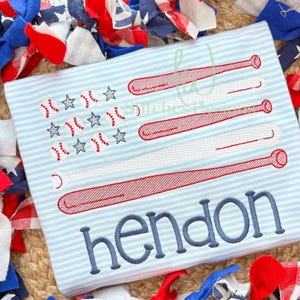 Puede incluir: Camiseta a rayas azul claro con un diseño bordado con temática de béisbol. El diseño presenta estrellas y pelotas de béisbol, junto con bates de béisbol rojos y blancos. El nombre "hendon" está bordado en escritura azul.