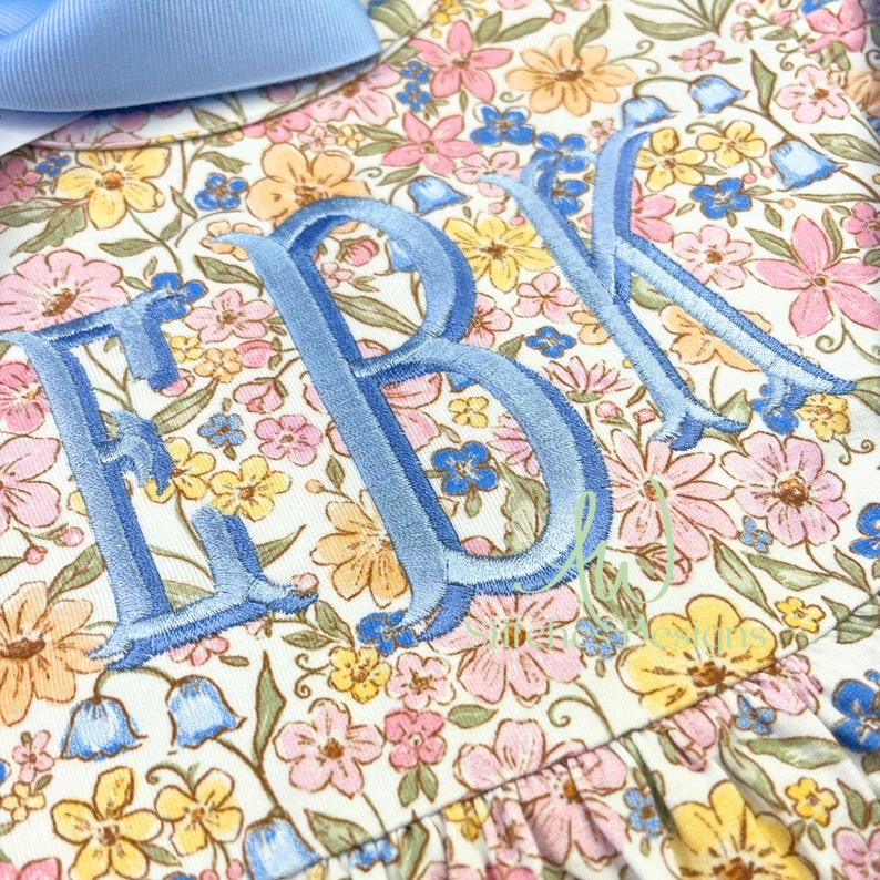 Peut inclure: Une robe blanche &agrave; imprim&eacute; floral avec les lettres brod&eacute;es bleues "EBK" sur le devant.