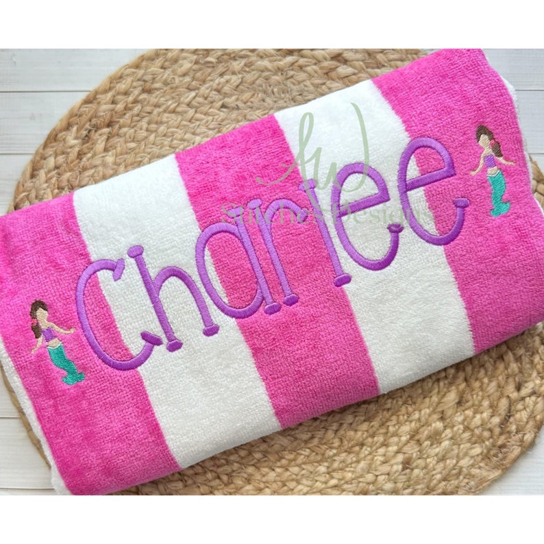 May include: Pink and white striped beach towel with the name "Charlee" embroidered in purple. Two small mermaid figures are embroidered on the towel.