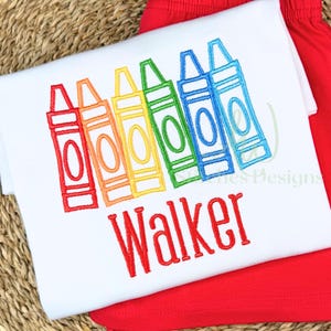 Embroidered design of colorful crayons with the name 'Walker' on a white fabric background.