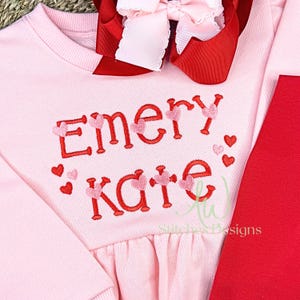 May include: Pink sweatshirt with red embroidered text that says "Emery Kate" with pink hearts around the text.
