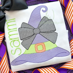 May include: A white shirt with a purple witch hat with a black bow and green trim. The text "Sammy" is embroidered on the shirt in green thread.