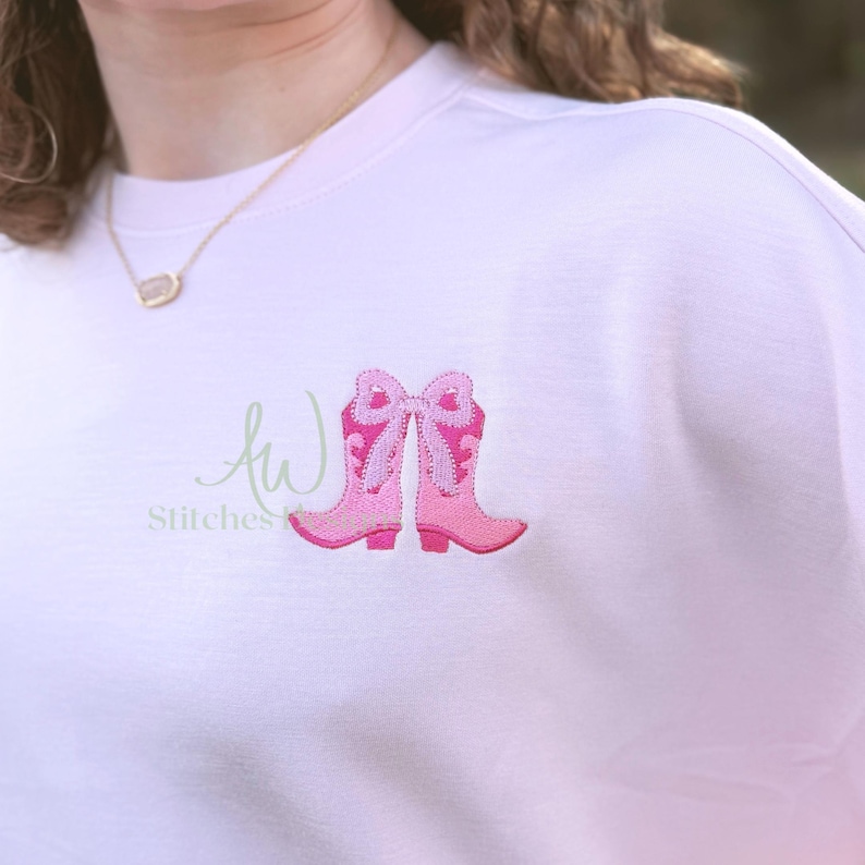 May include: Pink embroidered cowboy boots with a bow on a white sweatshirt.