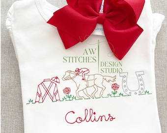May include: White onesie with red embroidery of a jockey riding a horse, a horseshoe, and a jockey's silks. The onesie also has the text "AW STITCHES DESIGN STUDIO" and "Collins" embroidered in red.