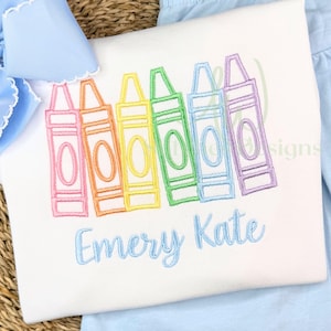 Embroidered shirt with colorful crayon design and 'Emery Kate' text on a pink background.