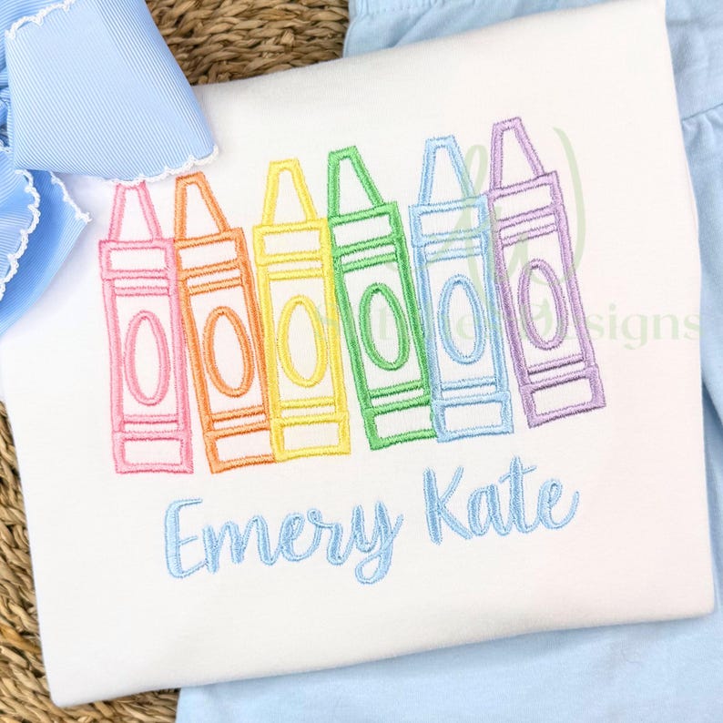 Embroidered shirt with colorful crayon design and 'Emery Kate' text on a pink background.