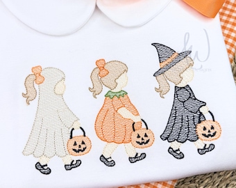 May include: A white shirt with a Peter Pan collar and an orange ribbon bow, featuring an embroidered design of three figures in Halloween costumes: a ghost, a pumpkin, and a witch, each carrying a small orange jack-o'-lantern candy bucket.