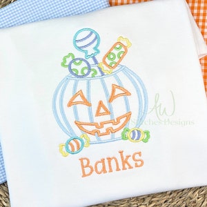 May include: A blue and orange embroidered design of a pumpkin with a smiling face, filled with candy and a lollipop. The text "Banks" is embroidered below the pumpkin.