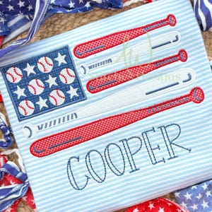 May include: Embroidered baseball-themed design on a light blue striped background. The design features a baseball flag with baseballs and stars, and baseball bats. The name "COOPER" is stitched in blue. Patriotic theme.