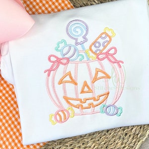 May include: A pastel pink and orange pumpkin with a smiling face is filled with colorful candy and lollipops. The pumpkin is surrounded by more candy, including a striped lollipop and a swirl lollipop.