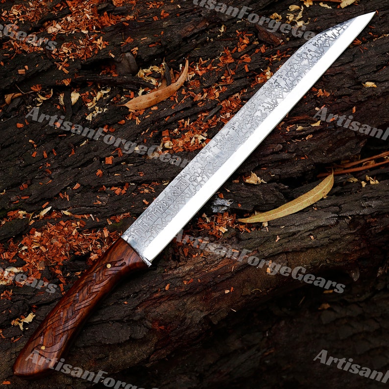 May include: A long, silver knife with a wooden handle. The blade has a hammered finish and is decorated with a pattern of runes. The handle is made of dark wood and has a braided design.