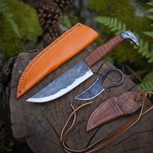 May include: A set of three handcrafted knives with leather sheaths. The largest knife has a brown leather-wrapped handle and a blade with a silver edge. The second knife is smaller with a curved blade. The third knife has a bird head design.