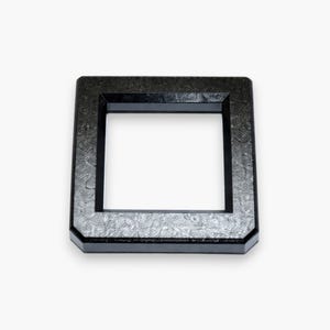 May include: A square, black, open-frame object with a textured surface. The frame has a rectangular opening in the center. The object is set against a white background.
