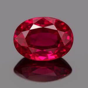 Könnte beinhalten: Ein facettierter, oval geschliffener Rubin-Edelstein. Der Edelstein hat eine tiefe, leuchtende rote Farbe mit zahlreichen Facetten, die das Licht reflektieren. Der Rubin liegt vor einem grauen Hintergrund, mit seinem Spiegelbild darunter.