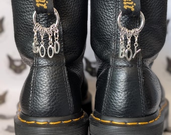 May include: Black leather platform boots with yellow stitching and silver charms that say "Good" and "Boy" hanging from the back of the boots. The boots have a chunky platform sole and a black leather upper.