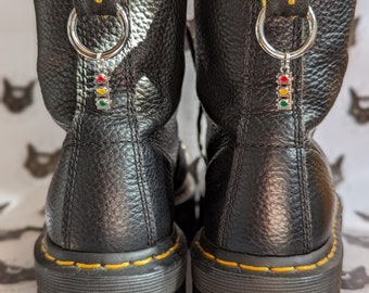 Könnte beinhalten: Schwarze Leder-Dr. Martens Stiefel mit gelben Nähten und einem silbernen Anhänger mit einem Ampel-Design. Die Stiefel haben eine dicke Plateau-Sohle.